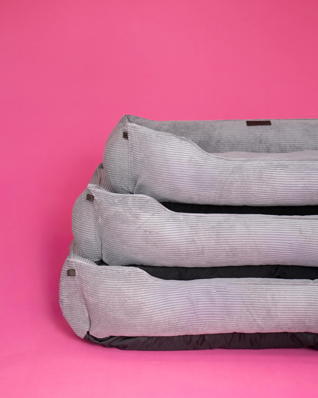 Three gray pet beds stacked on a pink background