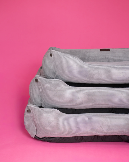 Three gray pet beds stacked on a pink background
